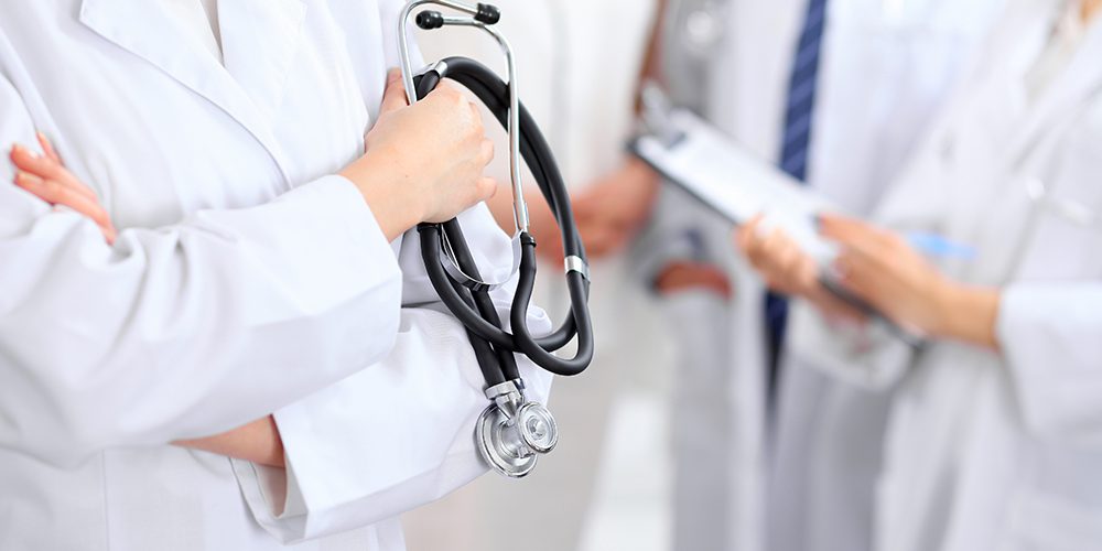 Female doctor holding a stethoscope in his hand, two doctors and patient are on the background